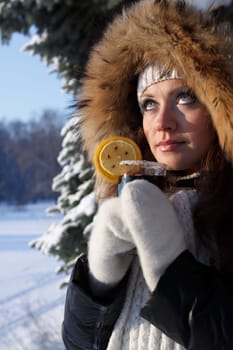 The beautiful girl drinks mulled wine in winter wood.