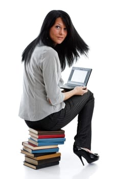 The attractive student sits on a pile of books with the laptop on a white background.