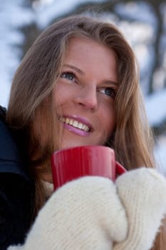 The beautiful girl with a cup of a hot drink in winter wood.