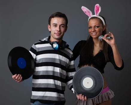 Male DJ and beautiful girl with vinyl disks on a grey background