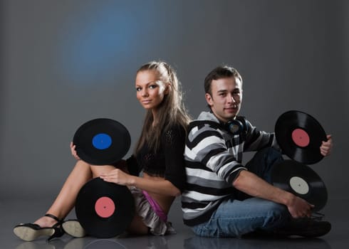 Male DJ and beautiful girl with vinyl disks on a grey background