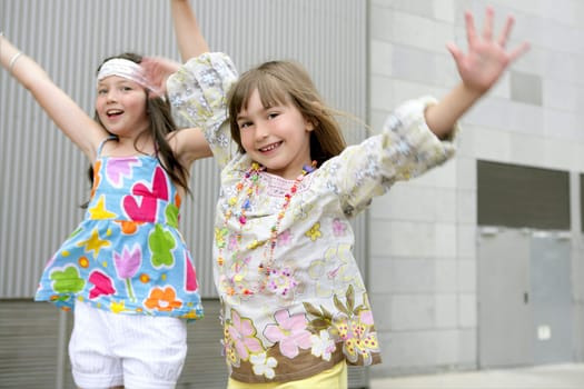 Two little girls dancing in the city with gray building in background
