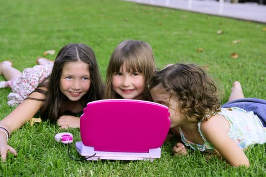 Three little girl outdoor playing with toy computer in grass