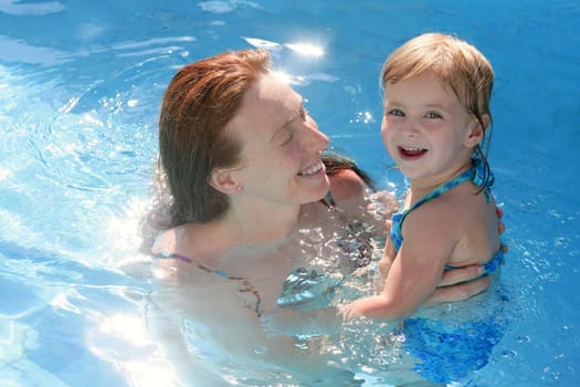 Blond daughter with redhead mother in blue swimming pool