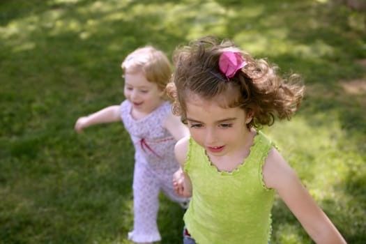 Beautifull little sisters running on the park over green grass