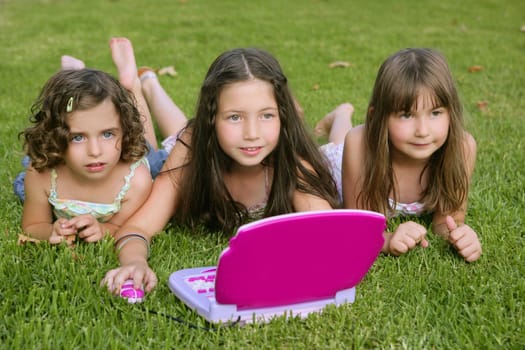 Three little girl outdoor playing with toy computer in grass