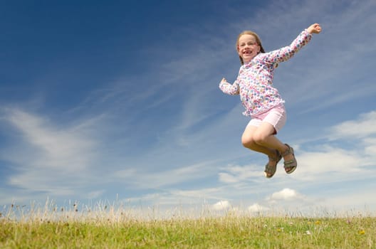 Young girl jumping on a green meadow against blue sky