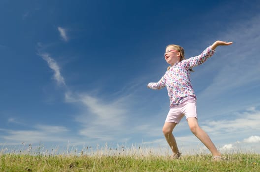 Young girl jumping on a green meadow against blue sky