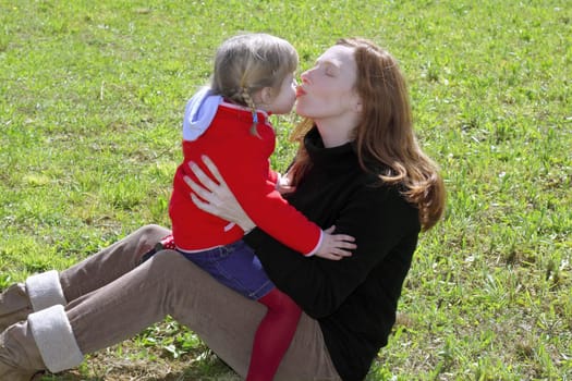 mother and daugther kissing mouth lips hug in winter meadow grass