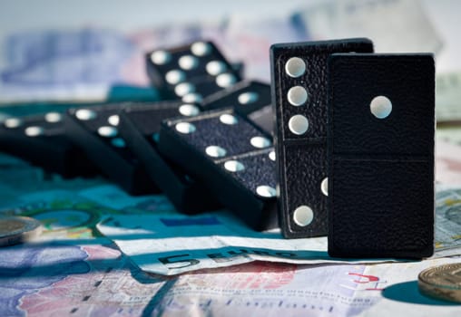 Fallen dominoes with blue harsh shadows on pound, euro and dollar bank notes illustrating banking crisis