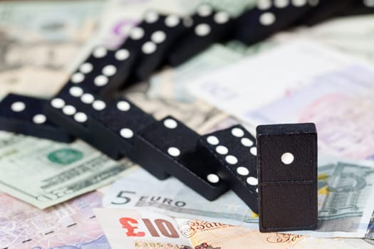 Fallen dominoes on pound, euro and dollar bank notes illustrating banking crisis
