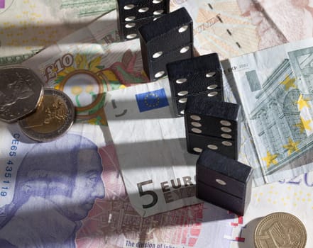 Standing dominoes with harsh shadows on pound, euro and dollar bank notes illustrating banking crisis