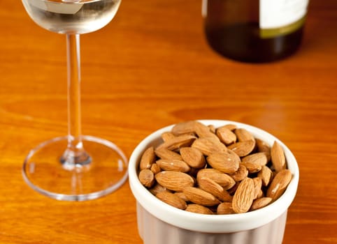 Pile of almond nuts in a porcelain bowl with glass and bottle of white wine