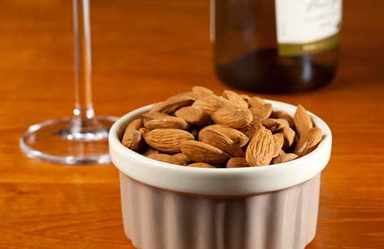 Pile of almond nuts in a porcelain bowl with glass and bottle of white wine
