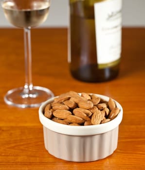 Pile of almond nuts in a porcelain bowl with glass and bottle of white wine