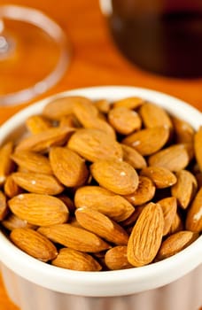 Pile of almond nuts in a porcelain bowl with glass and bottle of white wine