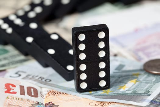 Fallen dominoes on pound, euro and dollar bank notes illustrating banking crisis