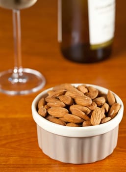 Pile of almond nuts in a porcelain bowl with glass and bottle of white wine