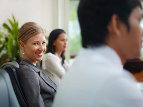 Beautiful young blonde woman working as manager and smiling at camera during business meeting with colleagues.