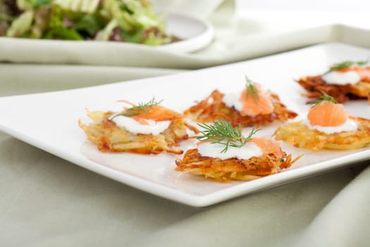 Bite sized potato rosti appetizer topped with fresh sour cream, smoked salmon and dill.