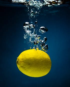 Fresh lemon in water on a black/blue background with air bubbles