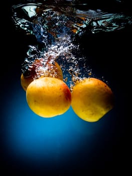 Fresh apricot in water on a black/blue background with air bubbles