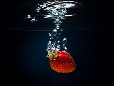 Fresh strawberries in water on a black/blue background with air bubbles