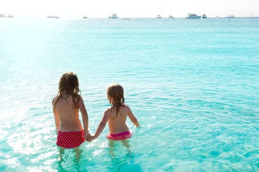 children girls rear view in the beach looking at sunset
