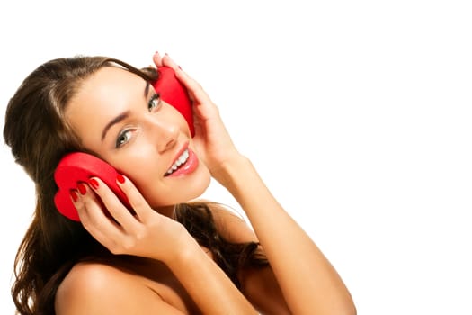 Beautiful woman holding heart-shaped box to her ears against white background