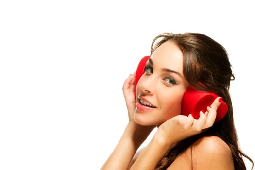 Beautiful woman holding heart-shaped box to her ears against white background