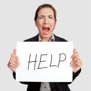 Stressed business woman imploring for help, holding a cardboard with the message "Help"". Focus is on the cardboard"
