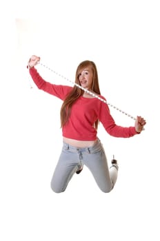 A teenage girl kneeling on the floor in jeans and a red sweater, holding a measuring tape, whit long brunette hair for white background.