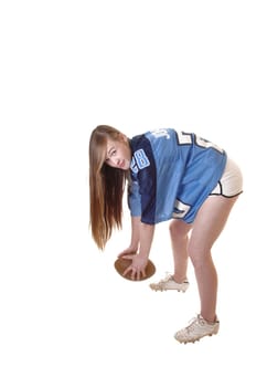 A young pretty girl in a football outfit and a football standing in the studio demonstrating how to play, with long brunette hair for white background.