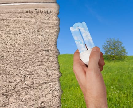 Glowing Energy Saving Bulb in Hand - Green Meadow and Dried Earth in Background