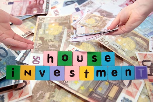 toy letters that spell house investment with cash in hands against a money background with clipping path
