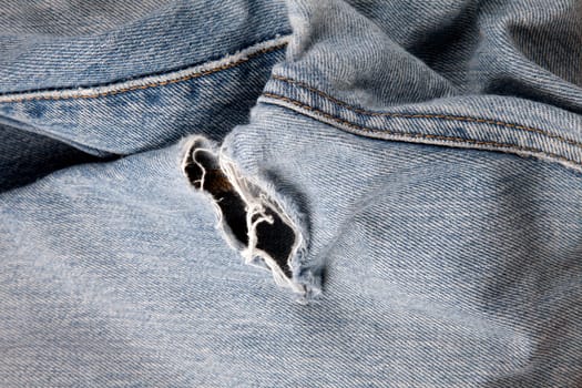 Close up of hole in an old pair of blue jeans showing the frayed threads.