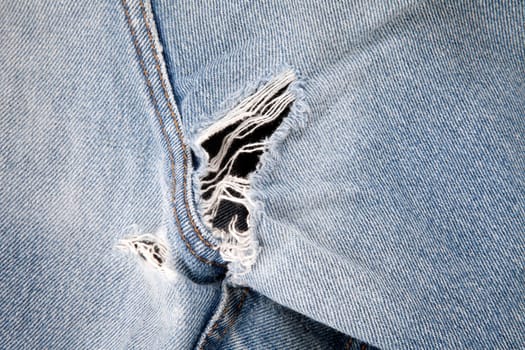 Close up of hole in an old pair of blue jeans showing the frayed threads.