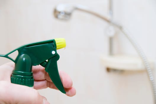 Hand with spray bottle in front of blurred handheld shower head in bright bathroom