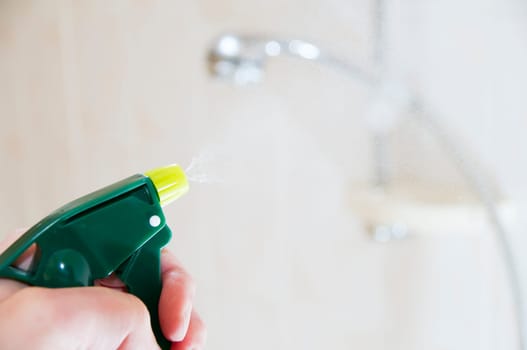 Hand with spray bottle in front of blurred handheld shower head in bright bathroom