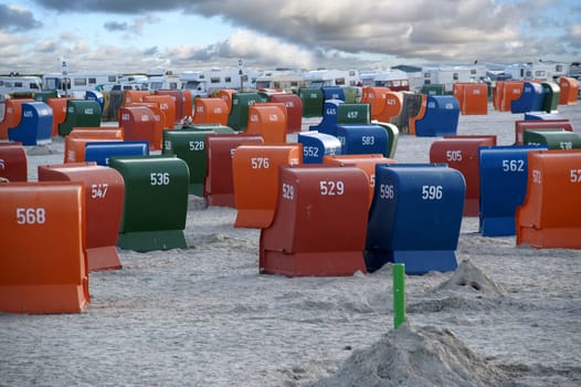 Beach chairs on the North Sea beach with cloudy sky and motorhomes in the background