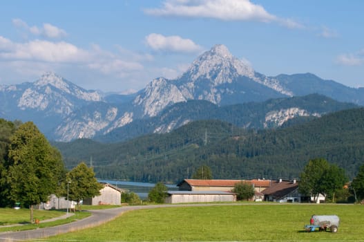 View over a pasture to a small farm in the Allgäu /Bavaria with alpine mountains in the background in summer in sunny weather with single clouds