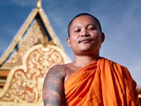 Mid adult Asian monk smiling at camera in buddhist monastery, Phnom Penh, Cambodia, Asia. Low angle