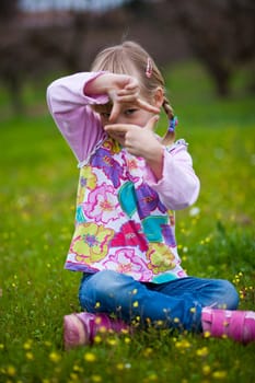 Cute little girl on a green field making a frame with fingers