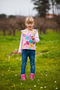 Cute little girl standing on a green field with flowers