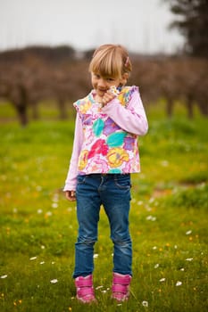 Cute little girl standing on a green field with flowers