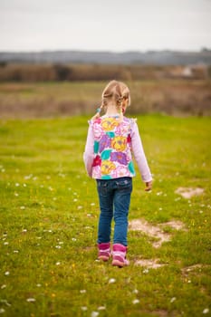 Cute little girl walking on a green field with flowers