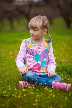 Cute little girl sitting on a green field with flowers