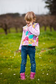 Cute little girl standing on a green field with flowers