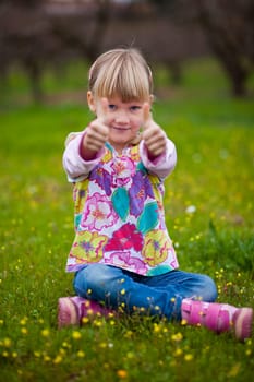 Cute little girl outdoors on a green field with thumbs up
