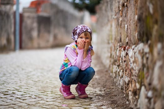 Portrait of a little girl outdoors on a city street, hands in front of mouth